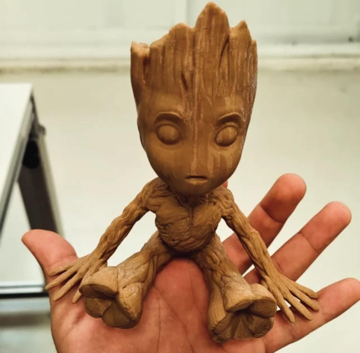 Mão segurando pequena figura marrom com textura de madeira e marcas de impressão 3D.