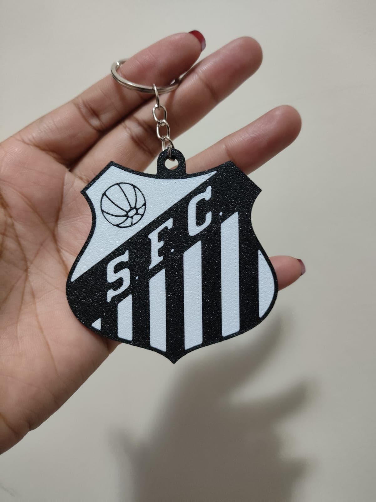 Chaveiro do Santos FC em preto e branco texturizado, segurado por uma mão.